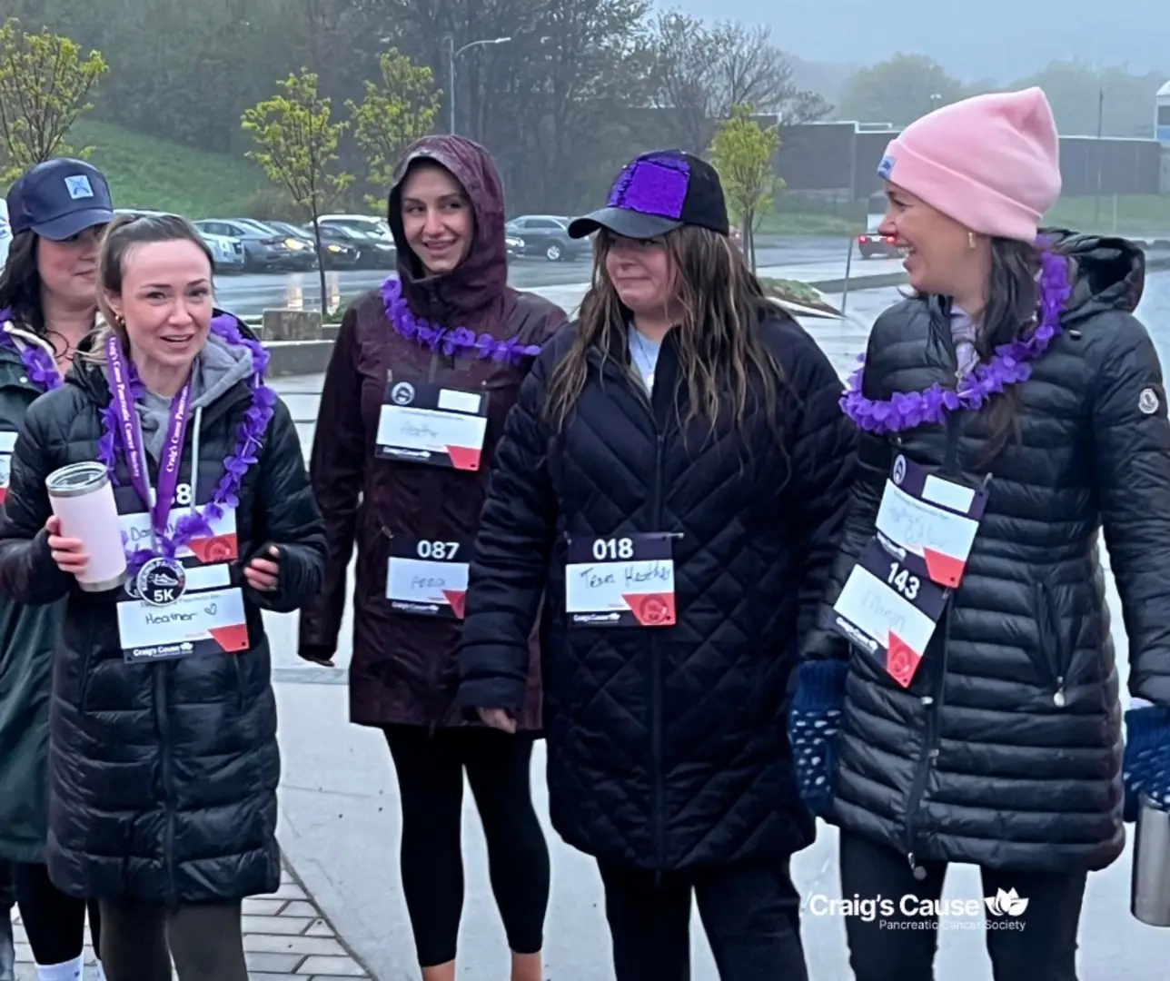 "Group of women wearing jackets and hats, participating in a 5K charity walk for Craig's Cause Pancreatic Cancer Society, smiling and supporting each other on a rainy day."