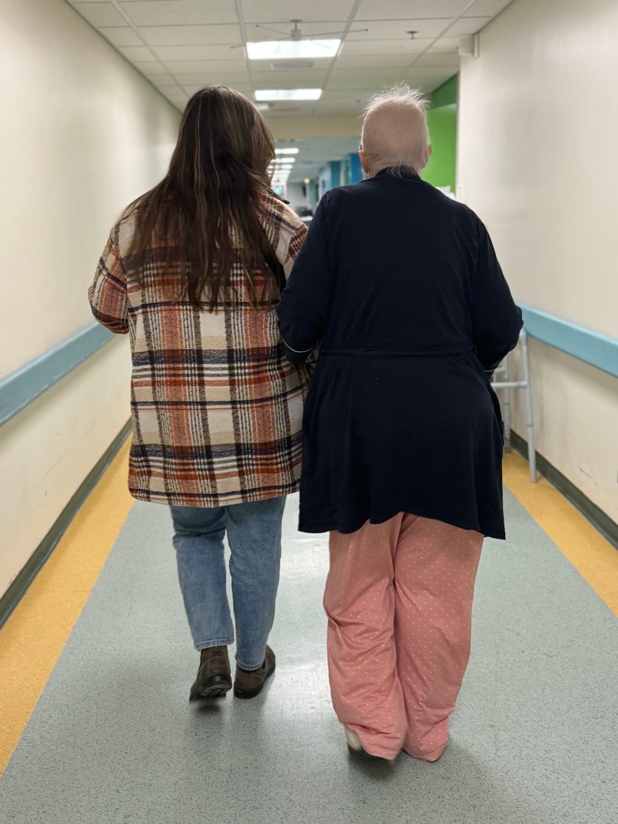 Mother and daughter walk hand in hand down a hospital hallway. 