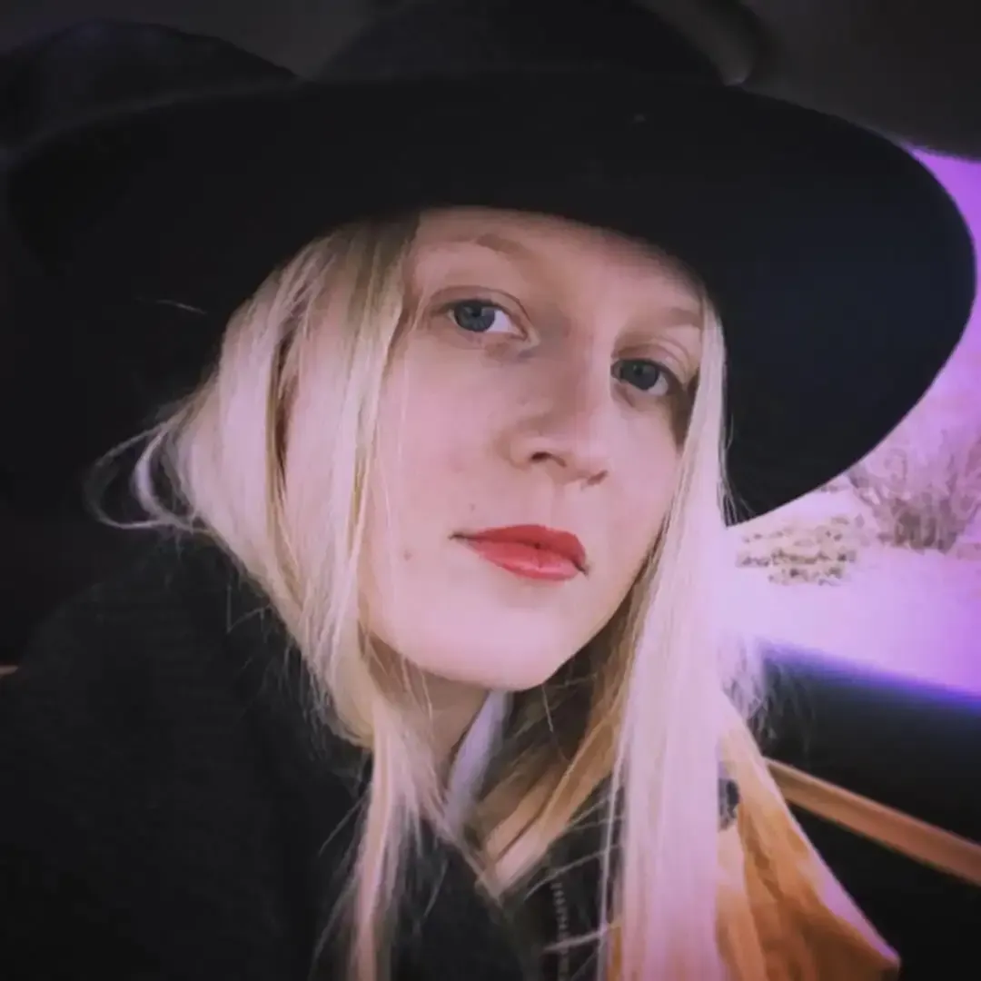 Close-up portrait of woman in black wide-brimmed hat and red lipstick against purple-tinted background in artistic lighting