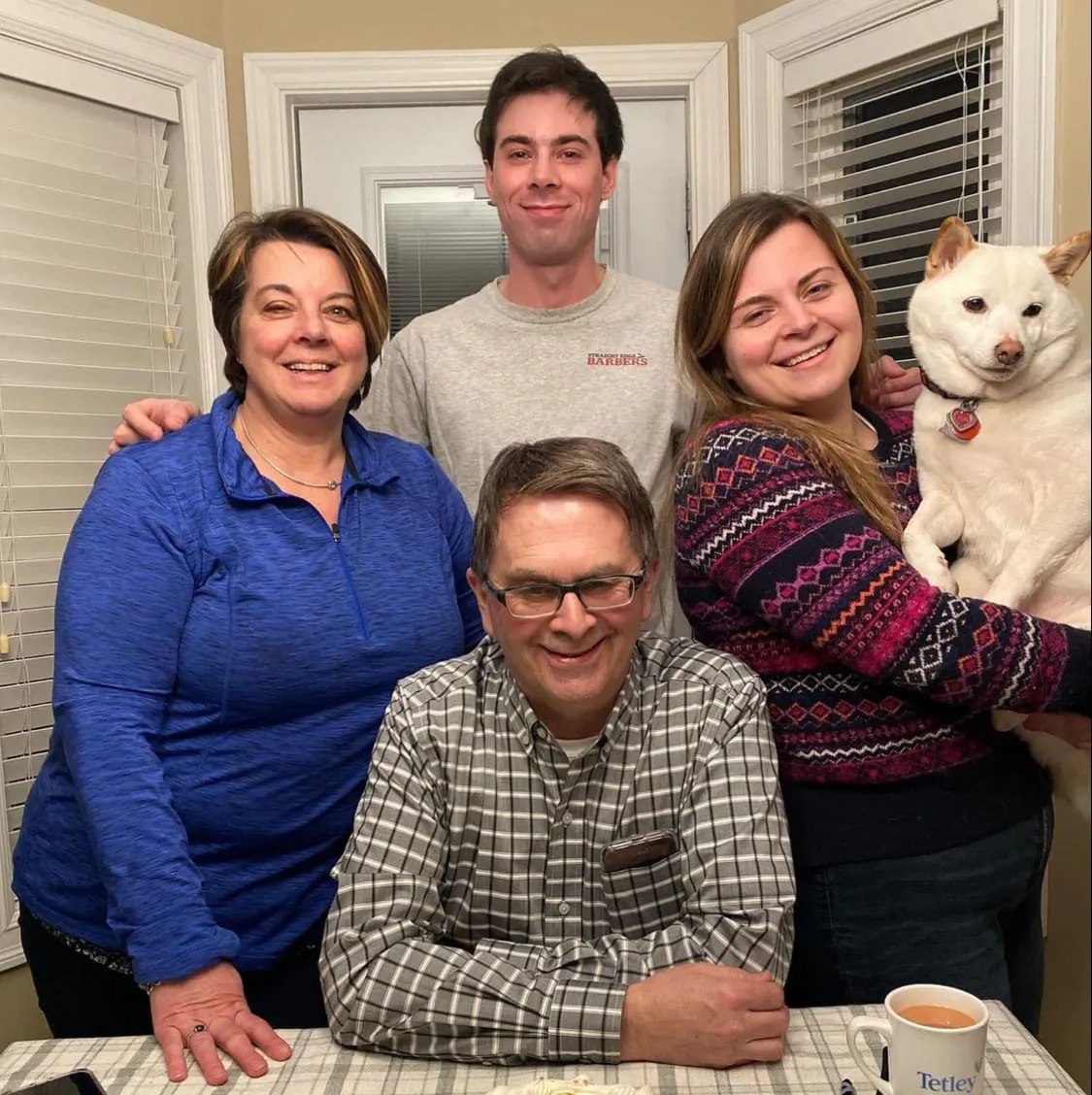 Cutler family of four smiling with their white dog Yuki, gathered around a table with a Tetley mug visible.
