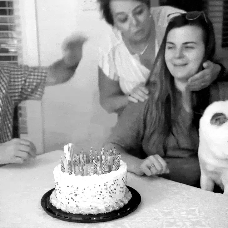 Black and white gif showing mother and daughter smiling over a birthday cake with sparkly decorations on a white tablecloth.