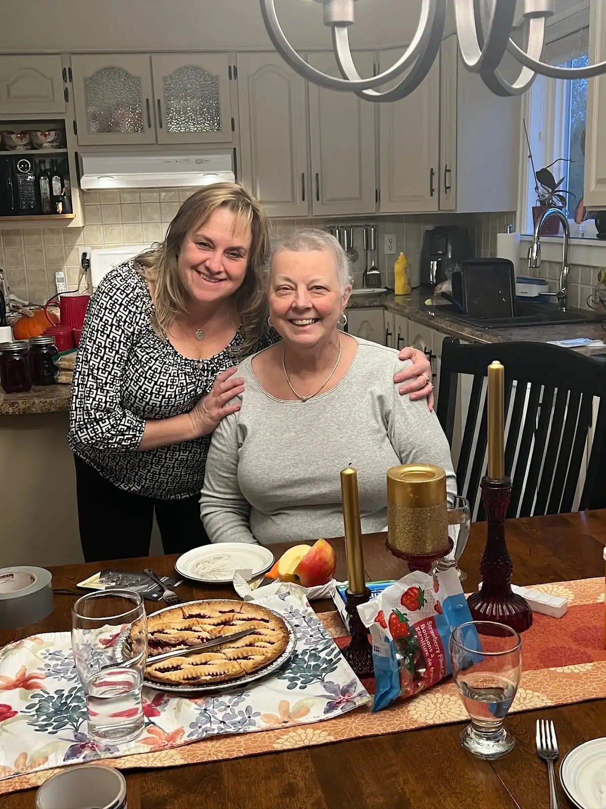 Bessie Ralph standing behind Heather Cutler at a dining table, both smiling, with dishes and a pie in the foreground.