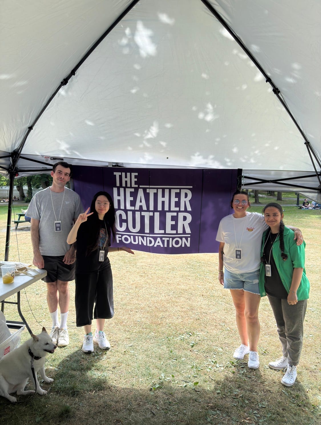 Christopher, Nhi, Lisa, and Kimia stand smiling under a canopy in front of The Heather Cutler Foundation banner with a white dog nearby.