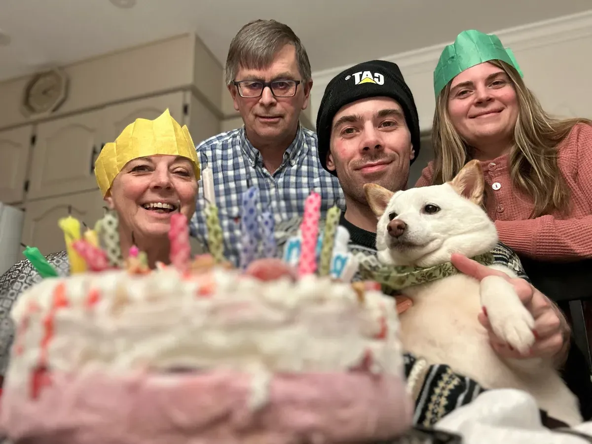 The Cutler family smile at the camera, their colorful party hats adding a festive touch as they pose with their Shiba Yuki.