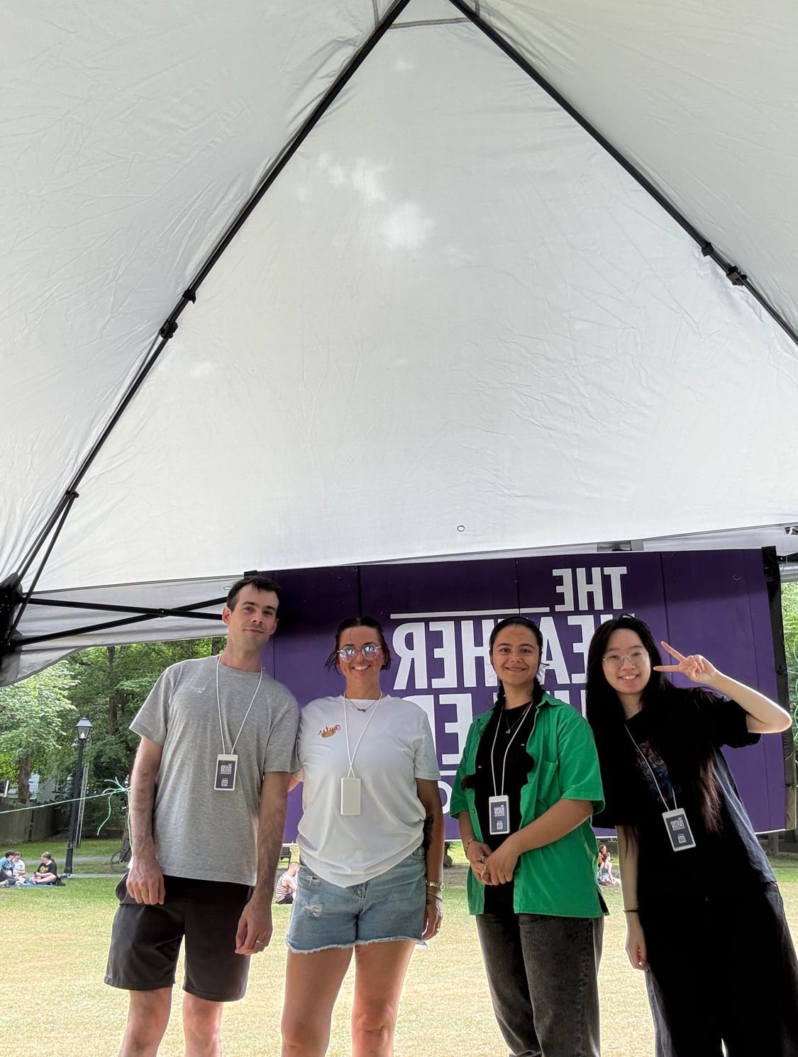 Four volunteers from The Heather Cutler Foundation smile under a canopy at Pride, standing in front of a purple banner.