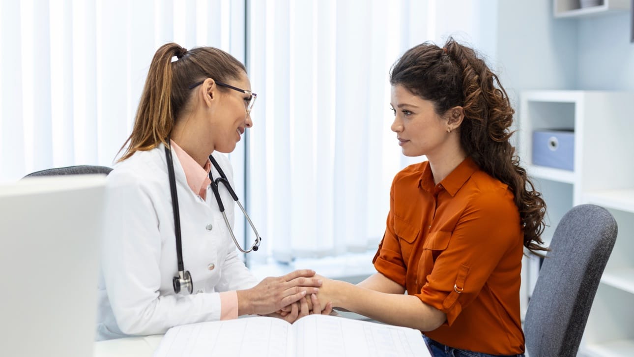 A doctor holding a patient's hands across a desk during a consultation