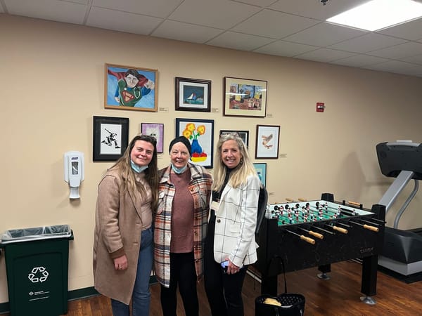 A mother, daughter and staff member of Johns Hopkins stand in a room decorated with colourful framed artworks on the wall.